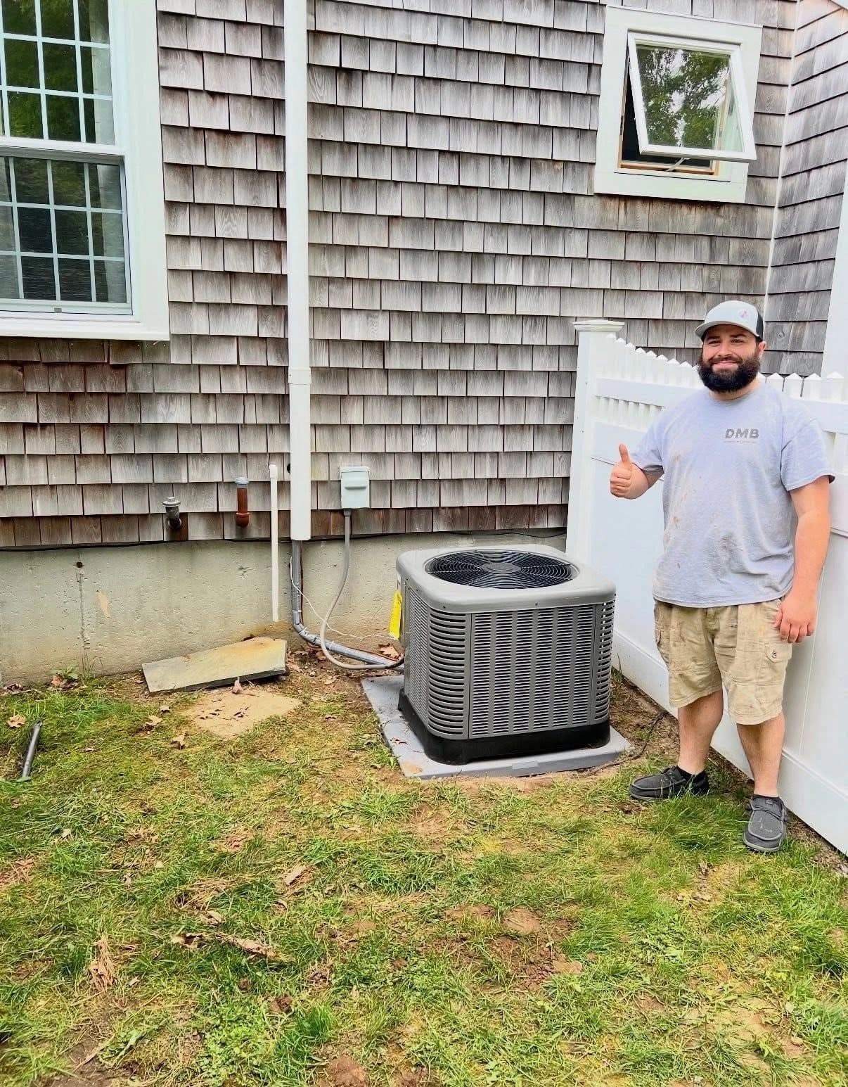 Dean Blanchard of DMB giving a thumbs up beside a new outdoor condenser at a shingled home