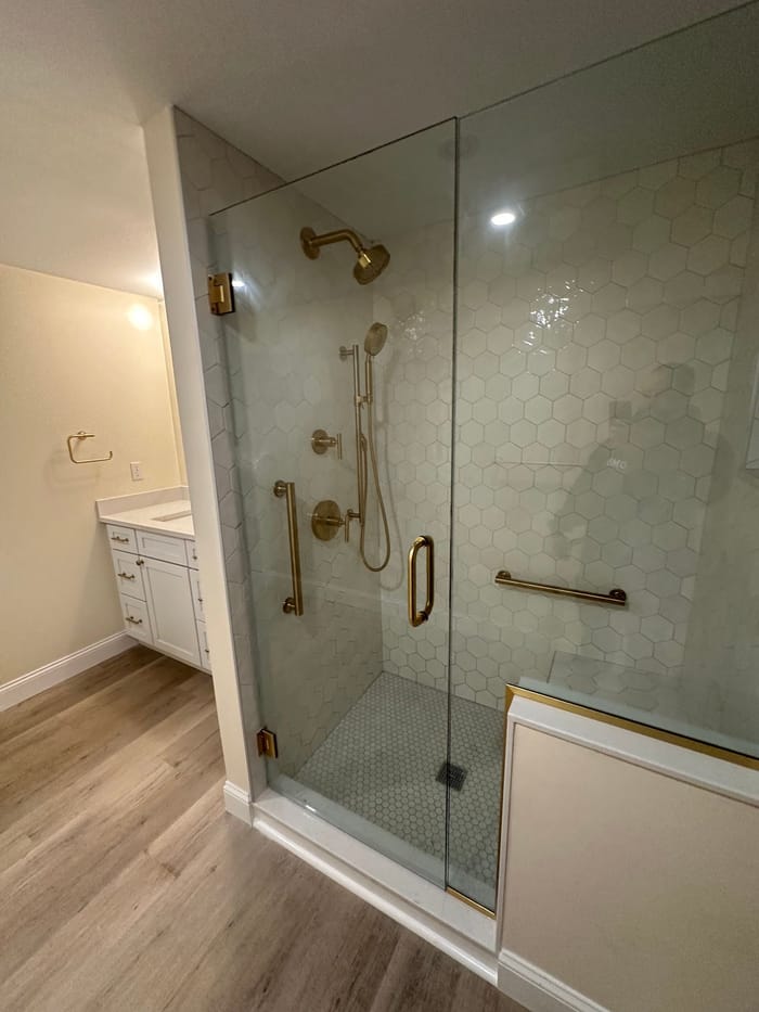 Glass shower with a brushed gold valve, shower head and grab bar